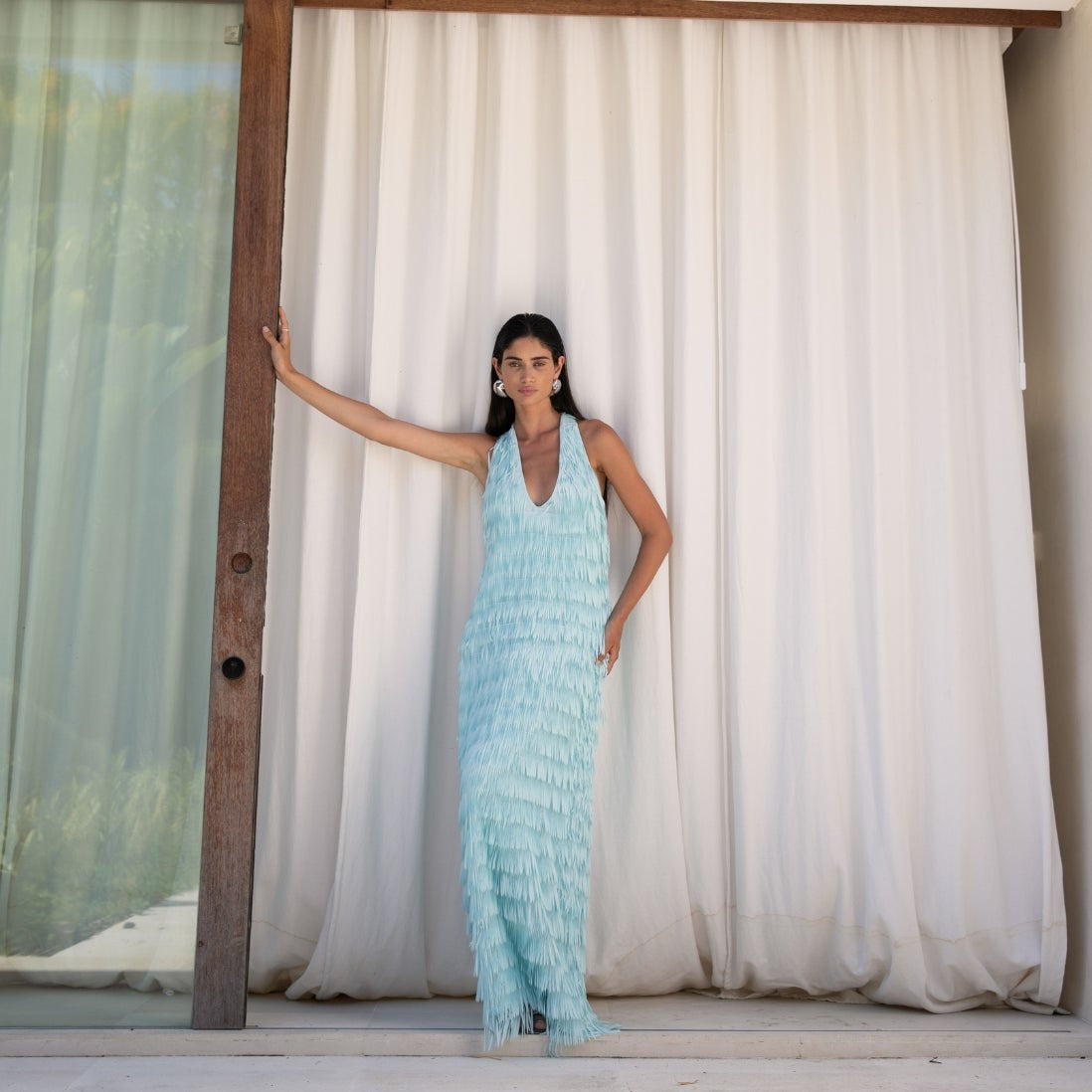 Woman in a light blue dress standing in front of a white curtain.